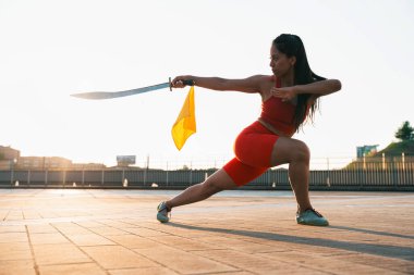 Chinese young woman practicing wushu kung fu with weapons outdoor. Young girl training martial arts form for the competition. clipart