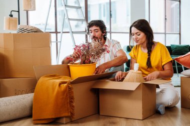 Mutlu genç çift yeni bir daireye taşınıyor. Genç bir kadın ve bir adam yeni aldıkları mülkte çalışıyor ve düzenliyor. Eşyaları ve kutuları birlikte taşımak. Yeni bir hayata ve emlak işine başlamak için yaşam tarzı kavramı.