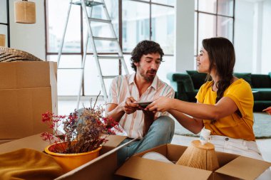 Mutlu genç çift yeni bir daireye taşınıyor. Genç bir kadın ve bir adam yeni aldıkları mülkte çalışıyor ve düzenliyor. Eşyaları ve kutuları birlikte taşımak. Yeni bir hayata ve emlak işine başlamak için yaşam tarzı kavramı.