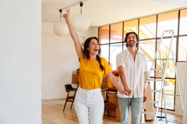 Mutlu genç çift yeni bir daireye taşınıyor. Genç kadın ve erkek yeni aldıkları mülkü kutluyor ve dans ediyorlar. Eşyaları ve kutuları birlikte taşımak. Yeni bir hayata ve emlak işine başlamak için yaşam tarzı kavramı.