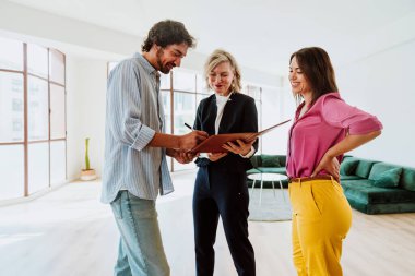 Emlakçı yeni bir daire gösteriyor ve genç bir çifte iyi bir yatırım yapıyor. Kadın ve erkek, şehrin zengin bir bölgesinde mülk satın alıyorlar. Sözleşmeyi imzalıyorum..