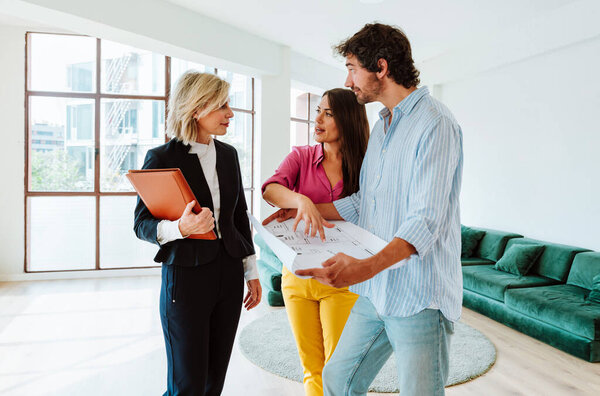 Агент по недвижимости показывает молодой паре новую квартиру и особенности хорошего инвестирования. Женщина и мужчина покупают недвижимость в богатом районе города.