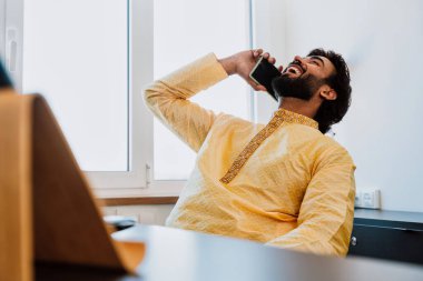 Pakistani Business man in the  office. Young business man with traditional outfit working in his office. Salesman Making a phone call with clients talking about new deals. clipart