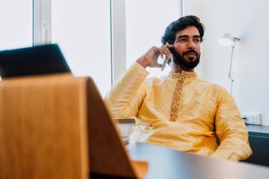 Pakistani Business man in the  office. Young business man with traditional outfit working in his office. Salesman Making a phone call with clients talking about new deals. clipart