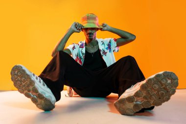 Renkli arka planda Afrikalı genç adam portresi - şık giyinen, yaratıcı renkli ışıklandırmalı havalı siyahi erkek