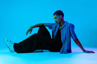 Renkli arka planda Afrikalı genç adam portresi - şık giyinen, yaratıcı renkli ışıklandırmalı havalı siyahi erkek