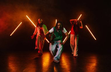 Bir grup hip hop dansçısı neon ışıklarıyla kasvetli bir stüdyoda dans ediyorlar..