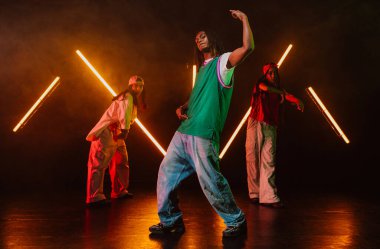 Bir grup hip hop dansçısı neon ışıklarıyla kasvetli bir stüdyoda dans ediyorlar..