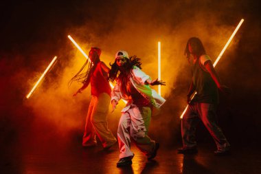 Bir grup hip hop dansçısı neon ışıklarıyla kasvetli bir stüdyoda dans ediyorlar..