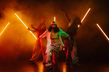 Bir grup hip hop dansçısı neon ışıklarıyla kasvetli bir stüdyoda dans ediyorlar..