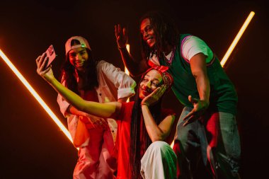 Hip hop dansçılarından oluşan bir grup, neon ışıklarıyla kasvetli bir stüdyoda dans ediyorlar. Ara verdiğimizde selfie çekiyoruz..