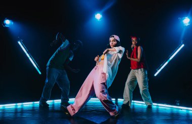 Bir grup hip hop dansçısı neon ışıklarıyla kasvetli bir stüdyoda dans ediyorlar..