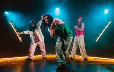 Bir grup hip hop dansçısı neon ışıklarıyla kasvetli bir stüdyoda dans ediyorlar..
