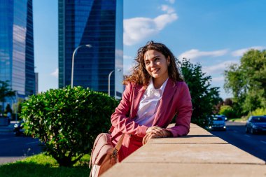 Şık takım elbiseli, güzel, genç bir iş kadını şehirde geziyor, neşeli, beyaz bir kadın ofiste çalışıyor.