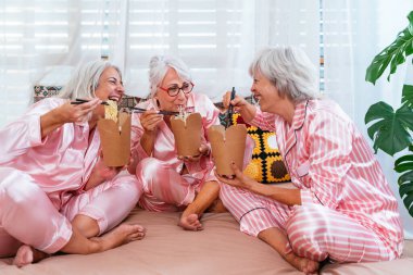 Evde komik pijama partisi veren güzel kadınlar, evde eğlenen, Asya eriştesi yiyen, yaşlılar, yaşam tarzı ve yaşam kalitesi konsepti olan neşeli yaşlı kadın arkadaşlar grubu.