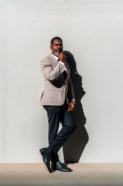 Şehirde gezen şık takım elbiseli, olgun siyahi işadamı, endüstriyel duvarda gri sakallı, üst düzey Afro-Afrikalı bir erkek.