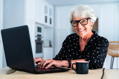 Güzel, yaşlı, beyaz saçlı, bilgisayar laptopu kullanan yaşlı bir kadın. Genç, yaşlı bir büyükanne evde kaliteli zaman geçiriyor.