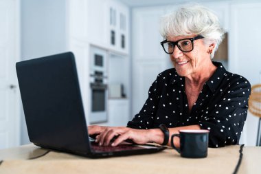 Güzel, yaşlı, beyaz saçlı, bilgisayar laptopu kullanan yaşlı bir kadın. Genç, yaşlı bir büyükanne evde kaliteli zaman geçiriyor.