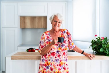 Gri saçlı, yaşlı, güzel bir kadın evde kahve içiyor genç, yaşlı bir büyükanne evde kaliteli zaman geçiriyor.