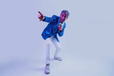 Stüdyoda poz veren kıdemli adam. Renkli arka planlarda poz veren pullu mavi ceketli komik son sınıf öğrencisi. Renkli jel ışıklarıyla stüdyo çekimi.