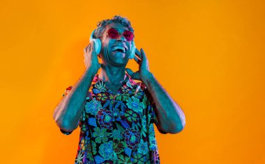 Stüdyoda poz veren kıdemli adam. Havai gömlekli, renkli arka planda poz veren komik bir son sınıf öğrencisi. Renkli jel ışıklarıyla stüdyo çekimi.