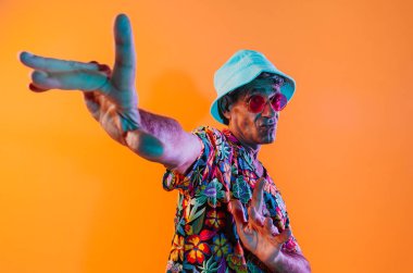 Stüdyoda poz veren kıdemli adam. Havai gömlekli, renkli arka planda poz veren komik bir son sınıf öğrencisi. Renkli jel ışıklarıyla stüdyo çekimi.