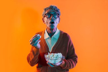 Stüdyoda poz veren kıdemli adam. Renkli arka planlarda poz veren ortalama kazaklı komik yaşlı bir adam. Renkli jel ışıklarıyla stüdyo çekimi.