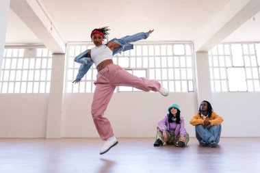 Çok ırklı hip-hop dansçılarından oluşan genç bir grup renkli sokak kıyafetleri giyip dans ediyorlar.