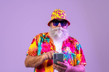 Stüdyoda gri sakallı, Hawaii gömlekli yaşlı bir adam komik stil sahibi, havalı tarzı telefon kullanan yetişkin bir turist, yaşlılar ve yaşam tarzı ile ilgili kavramlar.