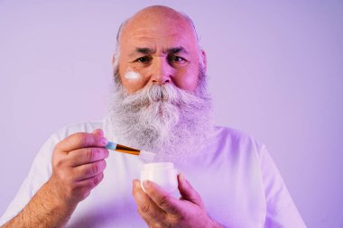 Stüdyoda gri sakallı yaşlı bir adamın güzellik portresi, yaşlı bir erkeğin cilt bakımını yapması, yaşlılar ve yaşam tarzı ile ilgili kavramlar.