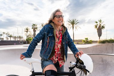 Şehir parkında bisiklet süren güzel bir son sınıf öğrencisi - Yetişkin bir bayan bisikletçi açık havada eğleniyor, yaşlılar, modern yaşam tarzı, sürdürülebilir ulaşım ve yeşil hareketlilik kavramları