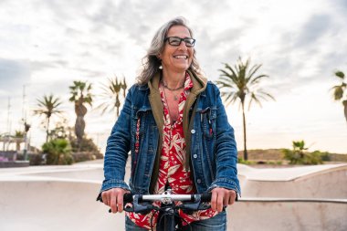 Şehir parkında bisiklet süren güzel bir son sınıf öğrencisi - Yetişkin bir bayan bisikletçi açık havada eğleniyor, yaşlılar, modern yaşam tarzı, sürdürülebilir ulaşım ve yeşil hareketlilik kavramları