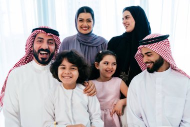 Suudi Arabistan kıyafeti giyen mutlu Arap ailesi akşam yemeği sırasında evde birlikte vakit geçiriyorlar - Orta Doğu Suudi aileleri ve çocukları Ramazan 'ı gün be gün kutluyorlar.