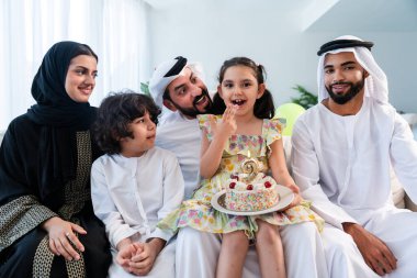 Emirati kıyafetleri içinde mutlu Arap ailesi evde birlikte vakit geçiriyorlar - Orta Doğulu ebeveynler ve çocuklar Dubai 'de modern bir dairede birbirlerine bağlanıyorlar doğum günlerini kutluyorlar
