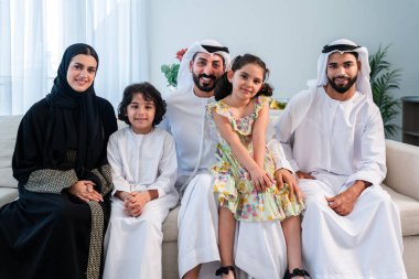 Emirati giysisi giyen mutlu Arap ailesi Dubai 'de modern bir dairede Orta Doğulu ebeveynler ve çocuklar olarak birlikte vakit geçiriyorlar.