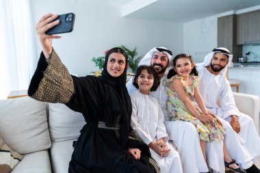 Emirati giysisi giyen mutlu Arap ailesi Dubai 'de modern bir dairede Orta Doğulu ebeveynler ve çocuklar olarak birlikte vakit geçiriyorlar.