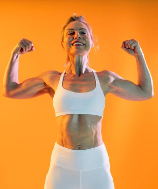 Güzel, olgun, spor kıyafetleri giyen spor giyinen bir kadın spor yapıyor. Sportif, olgun bir kadın spor kaslarını esnetiyor. Parlak bir arka plana karşı kaslarını esnetiyor.