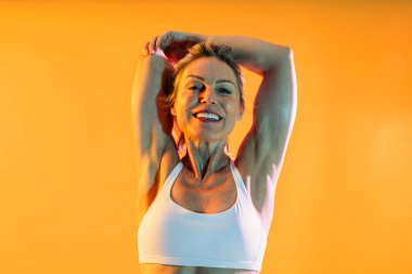 Spor kıyafetleri giyen güzel, olgun bir kadın spor giyer. Spor giyim sektöründe dinamik olgun bir kadın. Parlak, renkli bir arka plana karşı antrenman yapıyor.