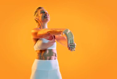 Güzel, olgun bir kadın spor kıyafetleri giyiyor spor yapıyor gülümsüyor spor kıyafetleri içinde kollarını turuncu bir arka plana doğru uzatan, sağlıklı ve aktif yaşlanmayı somutlaştıran yaşlı bir kadın.