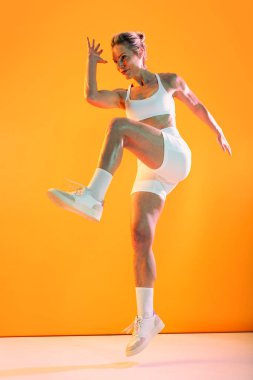 Güzel, olgun, spor kıyafetleri giyen spor kıyafetleri giyen, spor giyimli, enerjik, olgun bir kadın. Canlı turuncu bir zemine atlıyor. Kuvvetli ve formda.