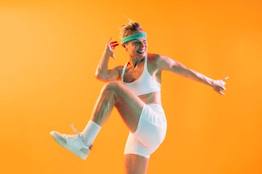 Spor kıyafetleri giyen, spor giyinen güzel olgun bir kadın spor giyimli, formda, olgun bir kadın canlı turuncu bir zemine karşı dinamik egzersizler yapıyor. Güç ve canlılık saçıyor.