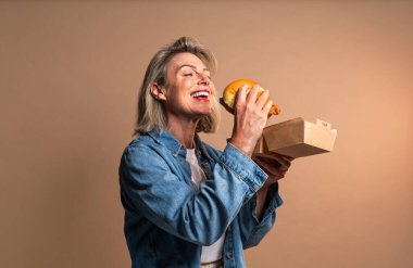 Renkli arka planda hamburger yiyen güzel olgun bir kadın elinde fast food sandviçi tutan orta yaşlı bir kadının portresi.