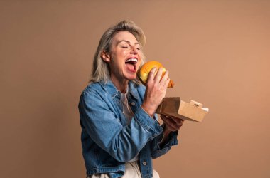 Renkli arka planda hamburger yiyen güzel olgun bir kadın elinde fast food sandviçi tutan orta yaşlı bir kadının portresi.