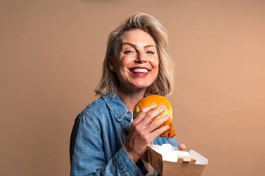 Renkli arka planda hamburger yiyen güzel olgun bir kadın elinde fast food sandviçi tutan orta yaşlı bir kadının portresi.