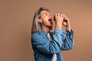 Renkli arka planda hamburger yiyen güzel olgun bir kadın elinde fast food sandviçi tutan orta yaşlı bir kadının portresi.