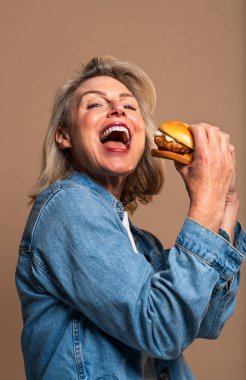 Renkli arka planda hamburger yiyen güzel olgun bir kadın elinde fast food sandviçi tutan orta yaşlı bir kadının portresi.