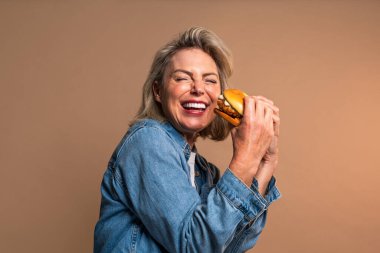 Renkli arka planda hamburger yiyen güzel olgun bir kadın elinde fast food sandviçi tutan orta yaşlı bir kadının portresi.