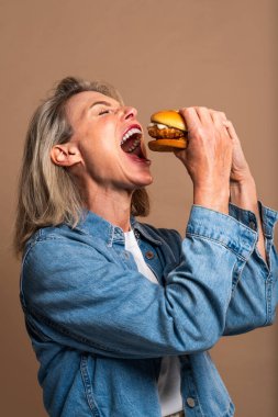 Renkli arka planda hamburger yiyen güzel olgun bir kadın elinde fast food sandviçi tutan orta yaşlı bir kadının portresi.