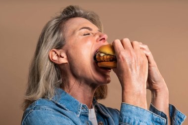 Renkli arka planda hamburger yiyen güzel olgun bir kadın elinde fast food sandviçi tutan orta yaşlı bir kadının portresi.