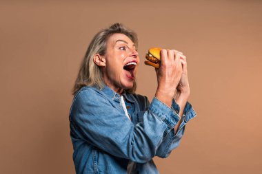 Renkli arka planda hamburger yiyen güzel olgun bir kadın elinde fast food sandviçi tutan orta yaşlı bir kadının portresi.